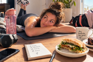 Mujer sudorosa relajándose después del gimnasio con sándwich y vino.