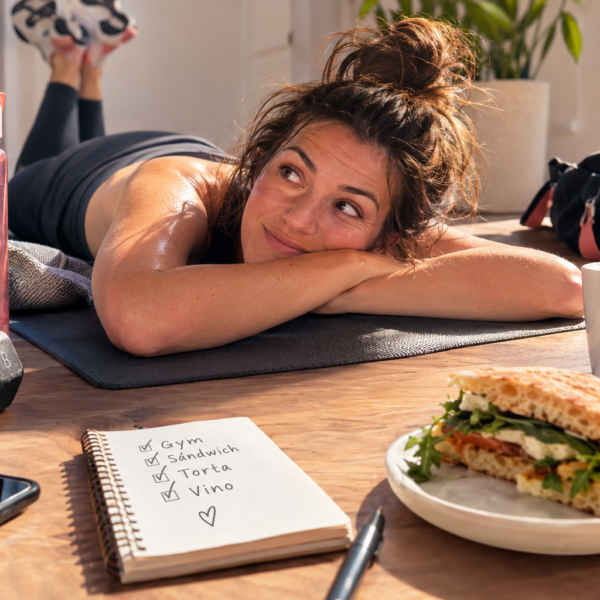 Historias - QuienQuisiera Mujer sudorosa relajándose después del gimnasio con sándwich y vino.